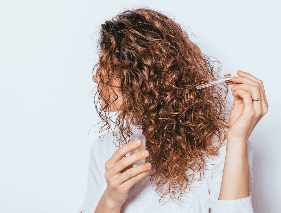 A woman with curly hair using a hair care product